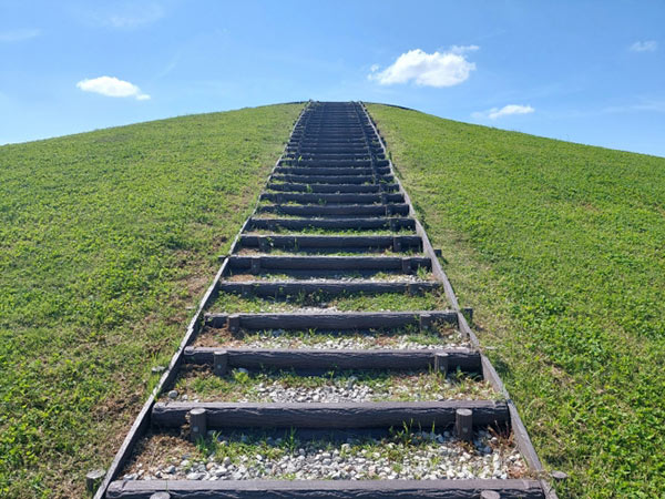 青空の広がる空に、丘の上に向かって伸びるまっすぐな階段。目的へのショートカットをイメージしてほしい画像。
