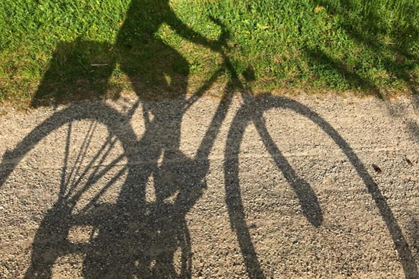 静かな道を進む自転車の影の写真。平坦ではない道だが、ゆっくりと自分のペースで進んでいくイメージ。