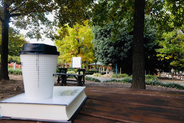 公園のテーブルに置かれたコーヒーと本の写真。焦りを手放し、静かな広々とした場所で落ち着いてみるイメージ。