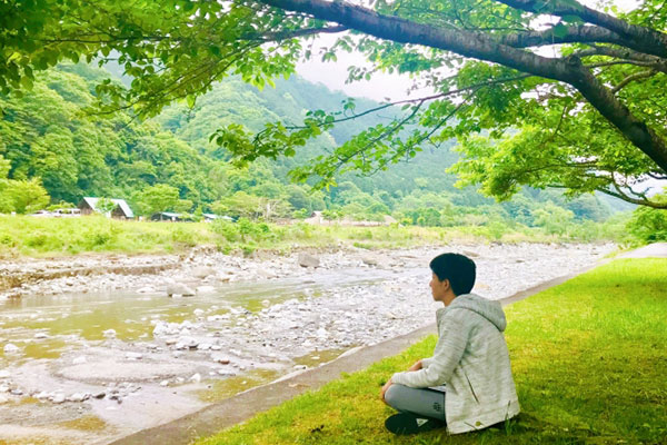 自然の景色が広がる川辺でくつろぐ写真。世間は動き続けているけれど、自然や世界・内なる自分はいつも寄り添ってくれているイメージ。